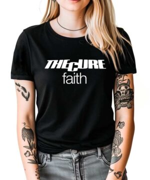 Kobieta z blond włosami i tatuażami na rękach w czarnej koszulce The Cure "Faith" na białym tle.
