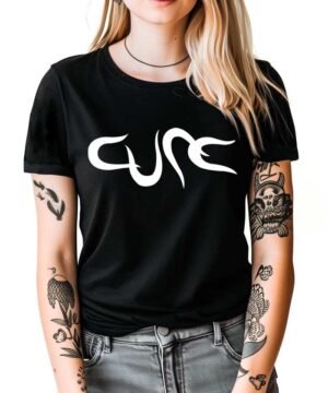 Czarna koszulka muzyczna The Cure z białym napisem "Cure", noszona przez osobę z blond włosami i tatuażami na ramionach.