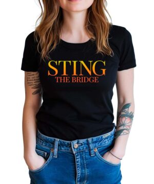 STING "The Bridge sign" czarna koszulka muzyczna z żółto-pomarańczowym napisem, męska, noszona do niebieskich jeansów.