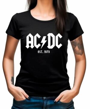 Kobieta ubrana w koszulkę ACDC "EST. 1973", czarna koszulka damska z białym napisem, stojąca z rękami w kieszeniach dżinsów.