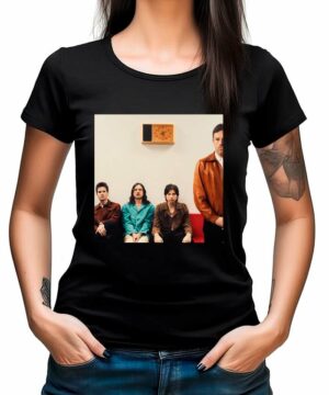 Czarna koszulka muzyczna KINGS OF LEON "Can we please have fun" z nadrukiem czterech osób pod zegarem na ścianie.