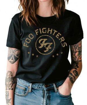 Osoba ubrana w czarną koszulkę Foo Fighters z nazwą i logo zespołu, z widocznymi tatuażami na obu ramionach i niebieskie dżinsy.