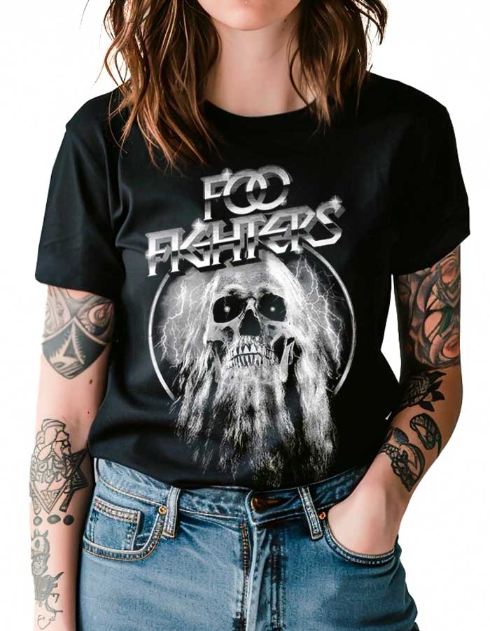tshirt-koncertowy-muzyczny-damski-foo-fighters-elder Osoba ubrana w czarną koszulkę damską FOO FIGHTERS "Elder" z motywem czaszki i błyskawicy, ręce w kieszeniach, widoczne tatuaże na ramionach.