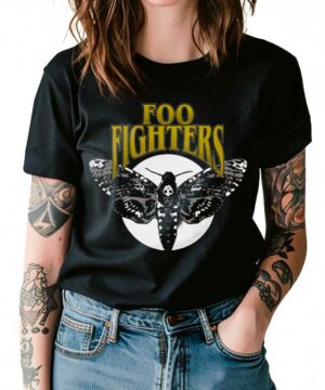 Osoba ubrana w czarną koszulkę damską FOO FIGHTERS "Hawk Moth" z napisem Foo Fighters nad dużą grafiką ćmy, stojąca z rękami w kieszeniach dżinsów.
