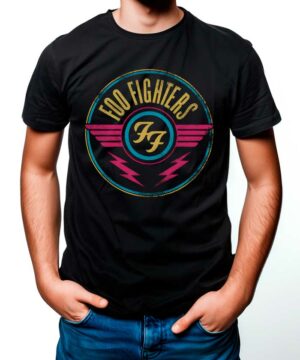 Osoba ubrana w koszulkę FOO FIGHTERS "Air" - czarną koszulkę z okrągłym logo zespołu, różowymi skrzydłami i dwiema różowymi błyskawicami - stoi swobodnie z rękami w kieszeniach.