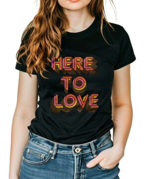 Czarna koszulka muzyczna LENNY KRAVITZ "Here to Love" z kolorowym napisem, kobieta ma rękę w kieszeni jeansów.