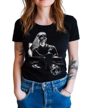 Kobieta nosząca koszulkę damską DEPECHE MODE "Fletch" - czarną koszulkę z czarno-białym wizerunkiem mężczyzny czytającego przy biurku i wydrukowanym podpisem poniżej.