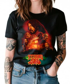 Osoba nosi czarną koszulkę damską FOO FIGHTERS "Studio 666" z ilustrowanymi twarzami członków zespołu i ognistym tłem, prezentując efektowne tatuaże na ramionach.