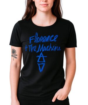 Osoba stoi twarzą do przodu, ubrana w koszulkę damską FLORENCE AND THE MACHINE "Hand drawn logo" - czarną koszulkę z Florence + The Machine i niebieskimi geometrycznymi wzorami z przodu.