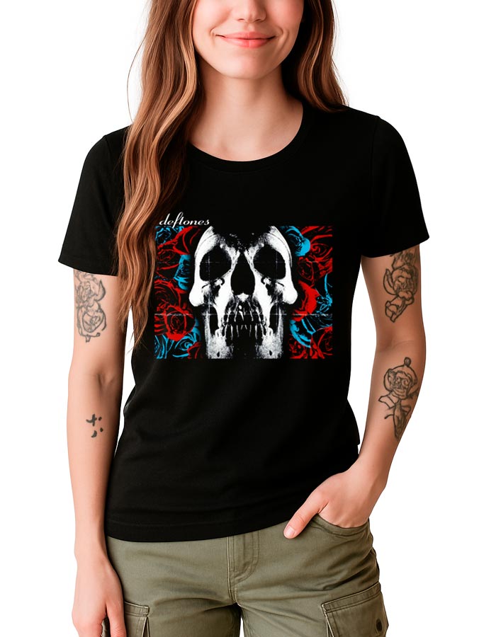 tshirt-muzyczny-damski-czarny-deftones-skull Kobieta ubrana w czarną koszulkę damską DEFTONES "Skull" z grafiką czaszki, czerwonych i niebieskich róż oraz napisem Deftones w lewym górnym rogu, stoi z jedną ręką w kieszeni.