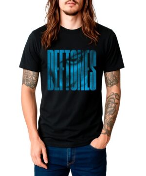 Osoba z długimi włosami i tatuażami nosi czarną koszulkę męską DEFTONES "Around the Fur halftone logo", stojąc pewnie z jedną ręką w kieszeni.