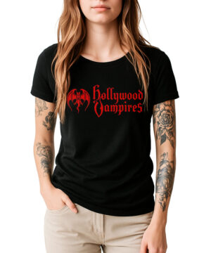 Kobieta o długich brązowych włosach i tatuażach na ramieniu prezentuje czarną damską koszulkę HOLLYWOOD VAMPIRES „Classic logo” z czerwonym napisem i grafiką przedstawiającą nietoperza. Stoi na białym tle z jedną ręką w kieszeni.